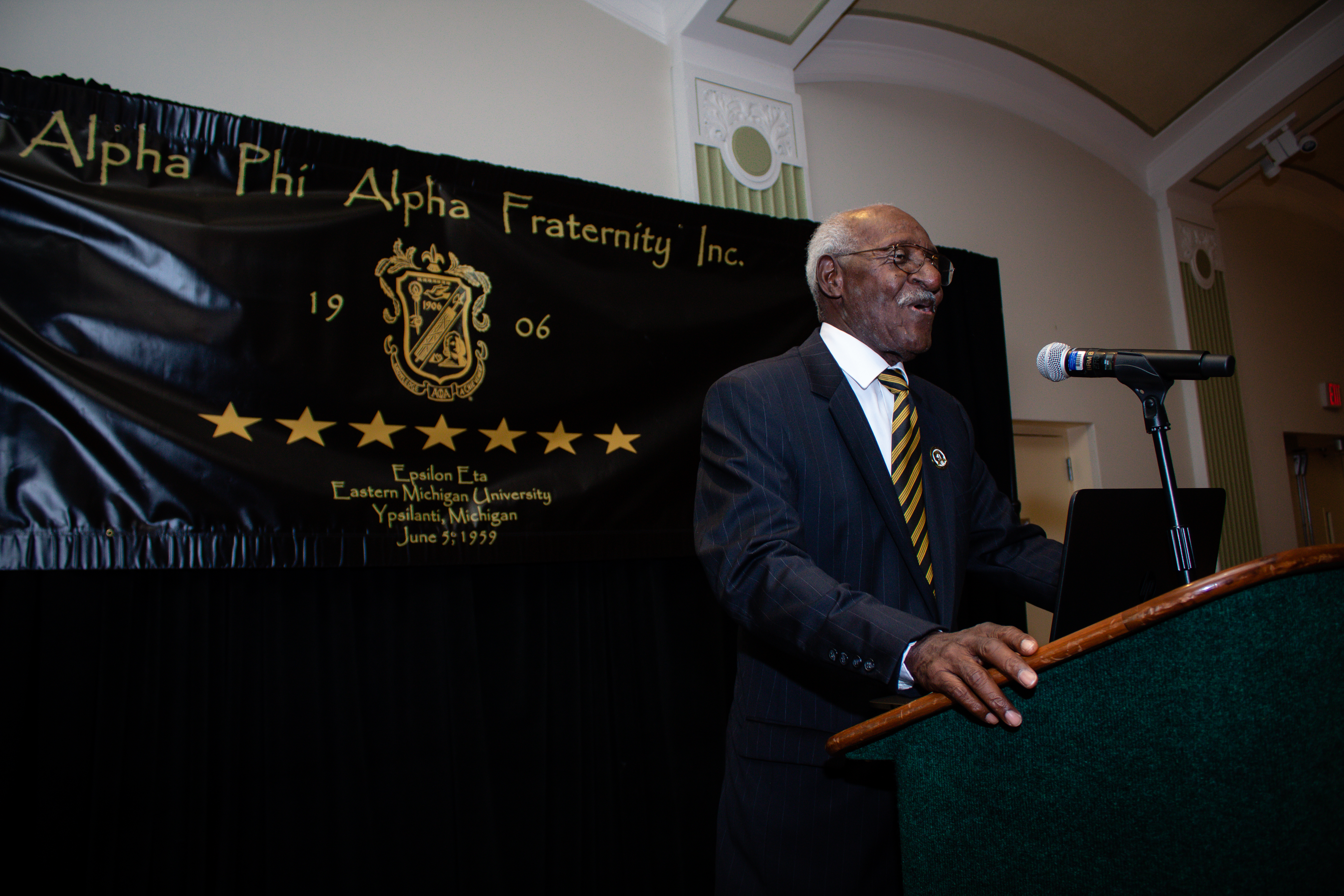 Epsilon Eta alumni speaker at a podium in front of an Alpha Phi Alpha banner