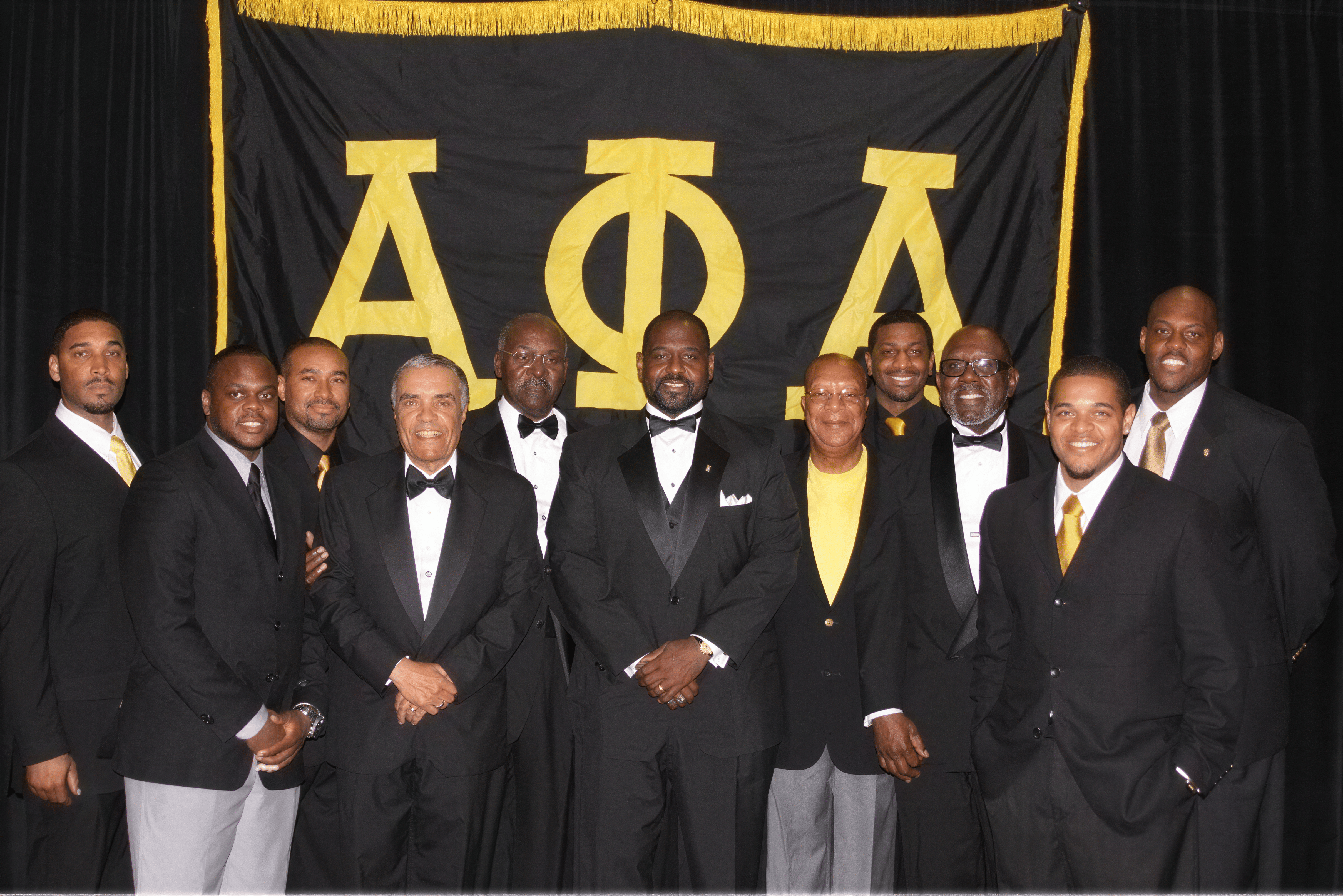 Group portrait of Epsilon Eta brothers standing in front of an Alpha Phi Alpha backdrop